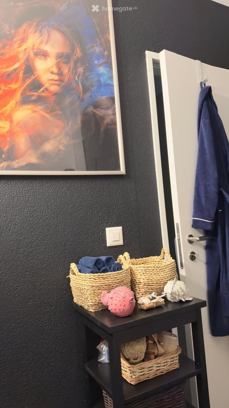 black wall, white door, table with baskets, picture frame, blue towel, pink object