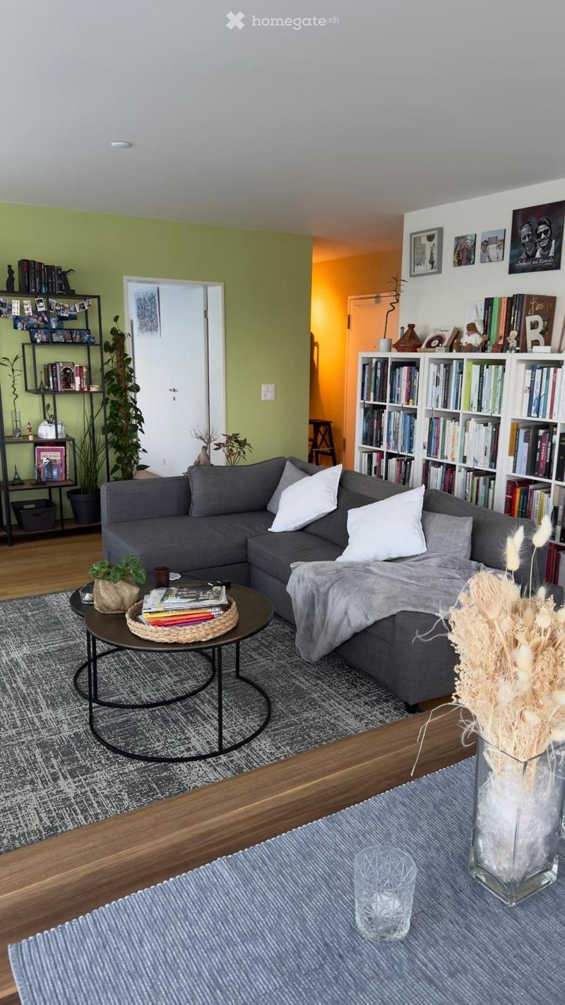 Living room with gray couch, round coffee table, bookshelves, plants, and a rug.