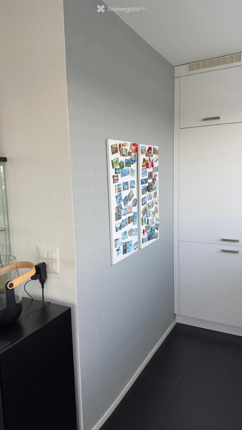 A wall with a collection of postcards, a power outlet, a black cabinet, and a white cabinet with drawers.