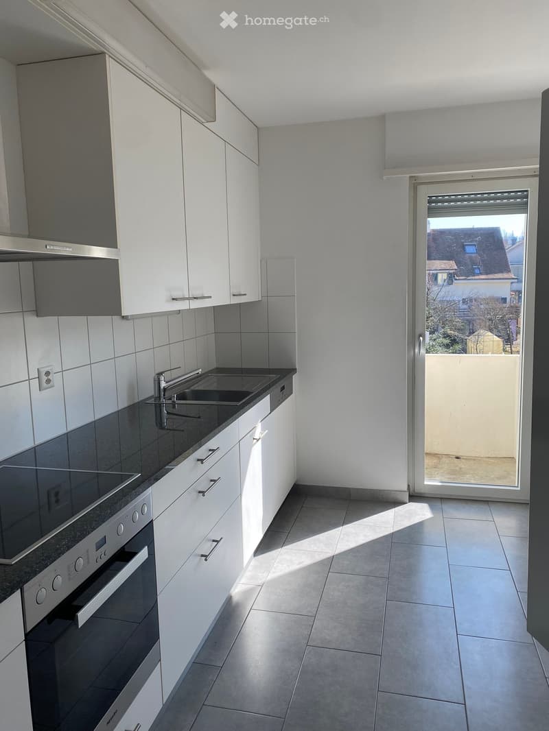 modern kitchen, white cabinets, black granite countertop, stainless steel sink, electric stove, oven, sliding door to balcony