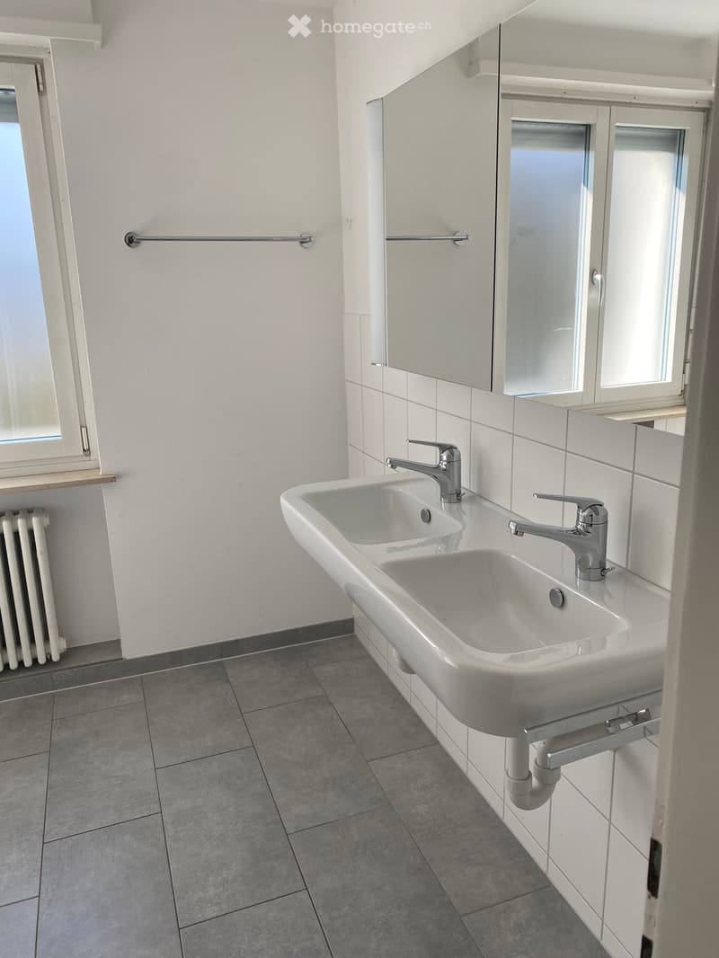 Bathroom with two sinks, mirror, radiator, tiled floor, and window