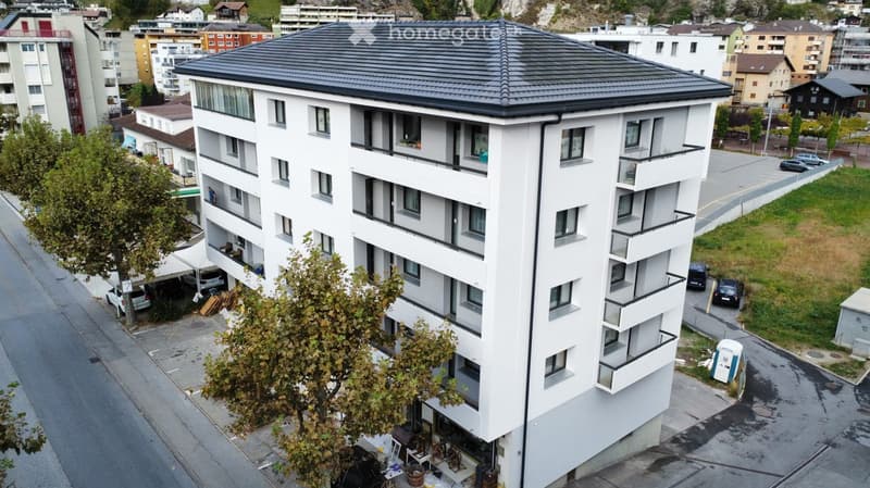 Modern white building with multiple floors, balconies, and a black roof