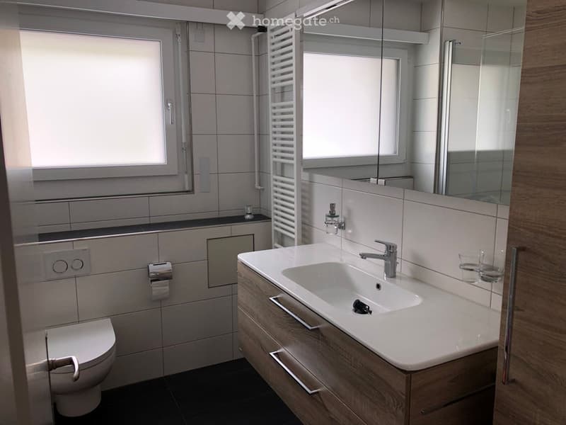 modern bathroom with white tiles, white sink, wooden cabinet, glass shower enclosure, toilet, towel rack