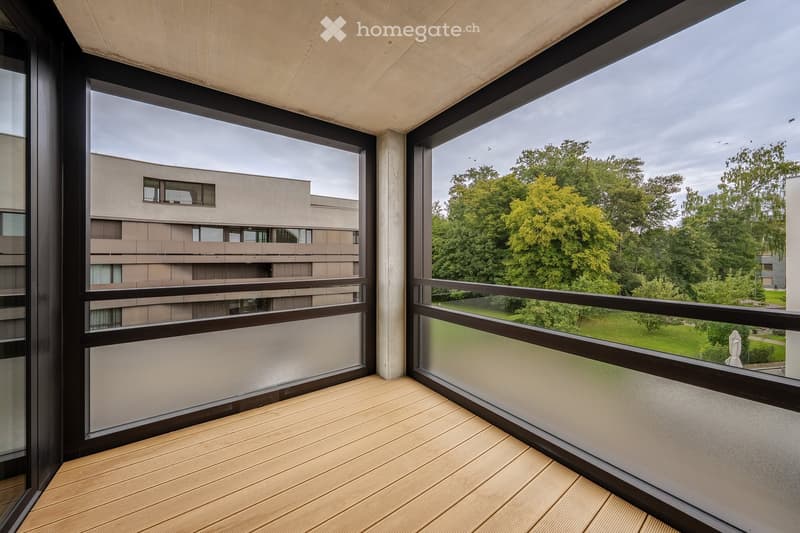 large balcony, large glass windows, wooden deck, modern building in background