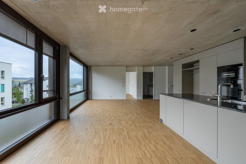 Modern kitchen with light wood flooring, white cabinets, black countertops, and large windows offering a view of the landscape.