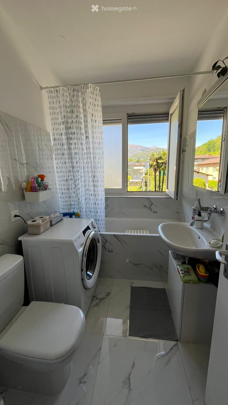 Bathroom with white marble tiles, bathtub, washing machine, sink, toilet, window with view