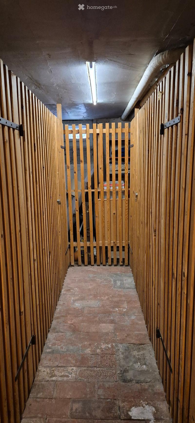 underground parking area, wooden walls, brick floor, metal railings, open gate