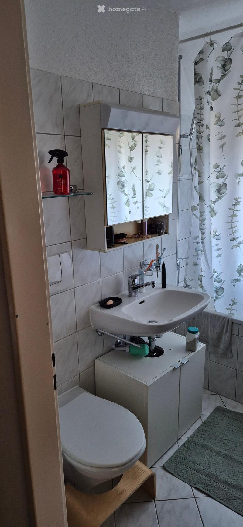 Bathroom with white tiles, white sink, white toilet, white cabinet, shower curtain, rug, and a red bottle on the shelf.