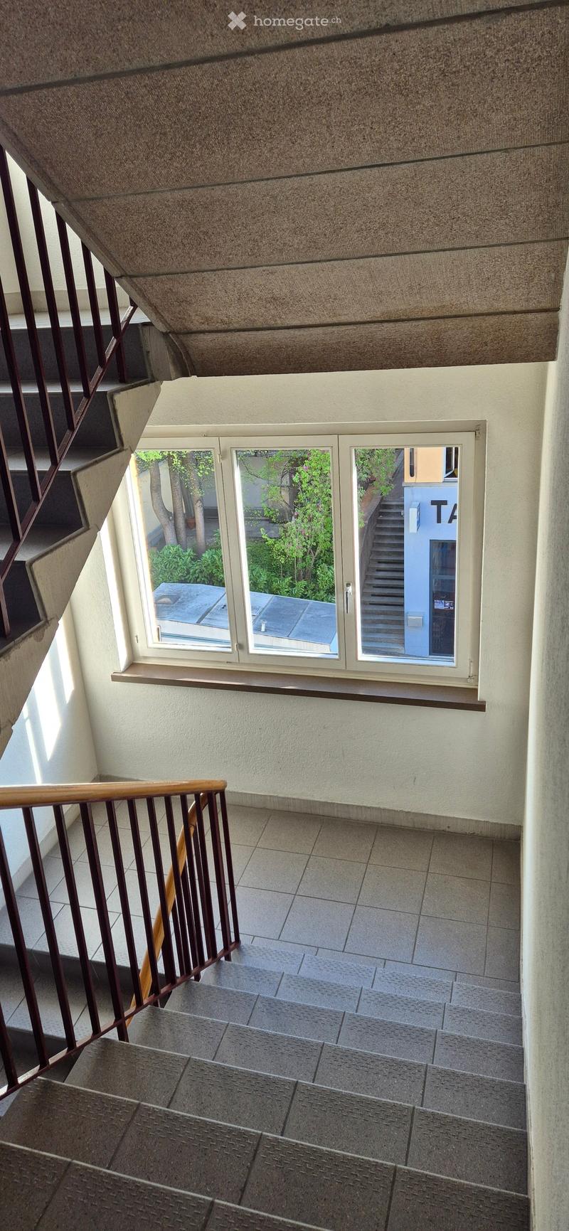 Staircase with tiled steps, wooden handrail, white walls, window with view of outside