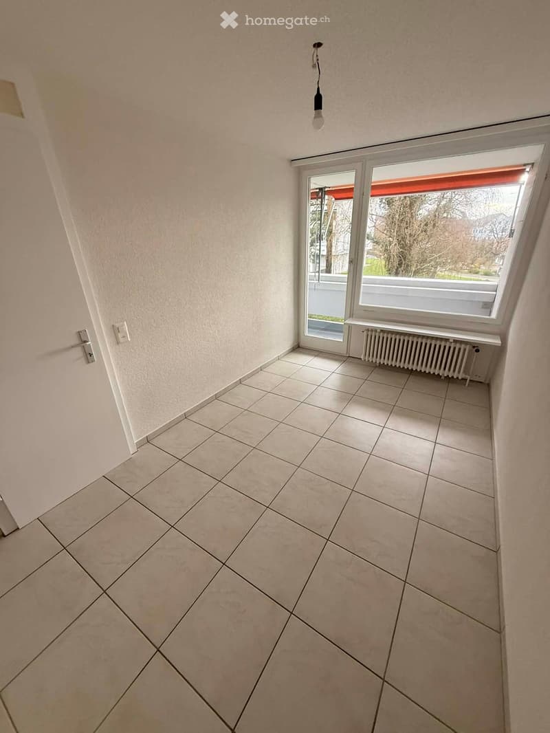 Empty room with white tiles, white door, white walls, large window, white radiator, light fixture