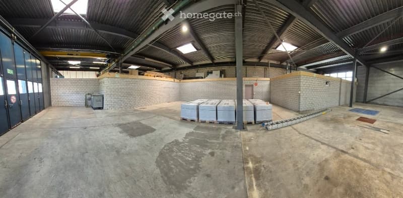 Empty warehouse with concrete floor, metal beams, brick walls, and storage boxes