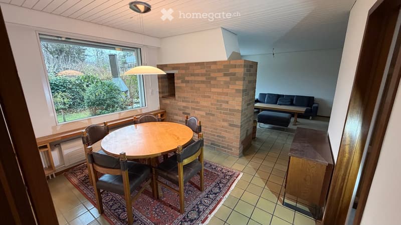 A round wooden table with chairs, a carpet, brick fireplace, and a window