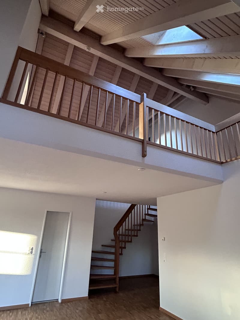 Spacious, modern staircase with wooden steps and railings, leading to an upper level with additional stairs visible in the background. Natural light streams in from skylights above.