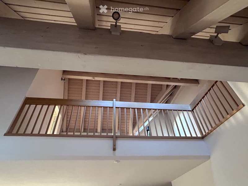 Open staircase with wooden railings and exposed wooden beams, modern lighting fixtures mounted on the ceiling.