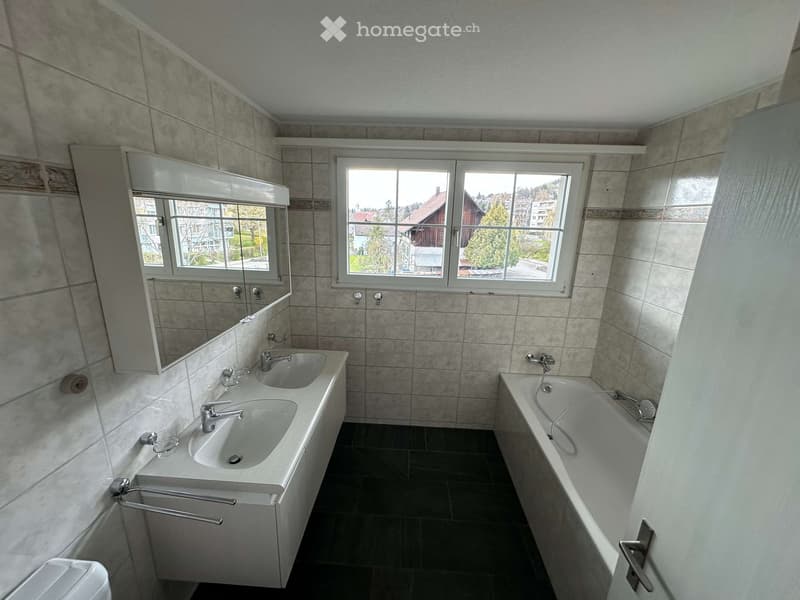 Bathroom with white tiles, a mirror, a sink with two faucets, a toilet, and a bathtub with a shower head.