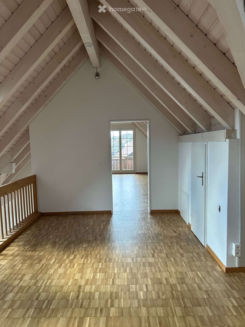 Empty attic room with wooden flooring, white walls, and wooden beams. There is a door leading to a balcony and a window.
