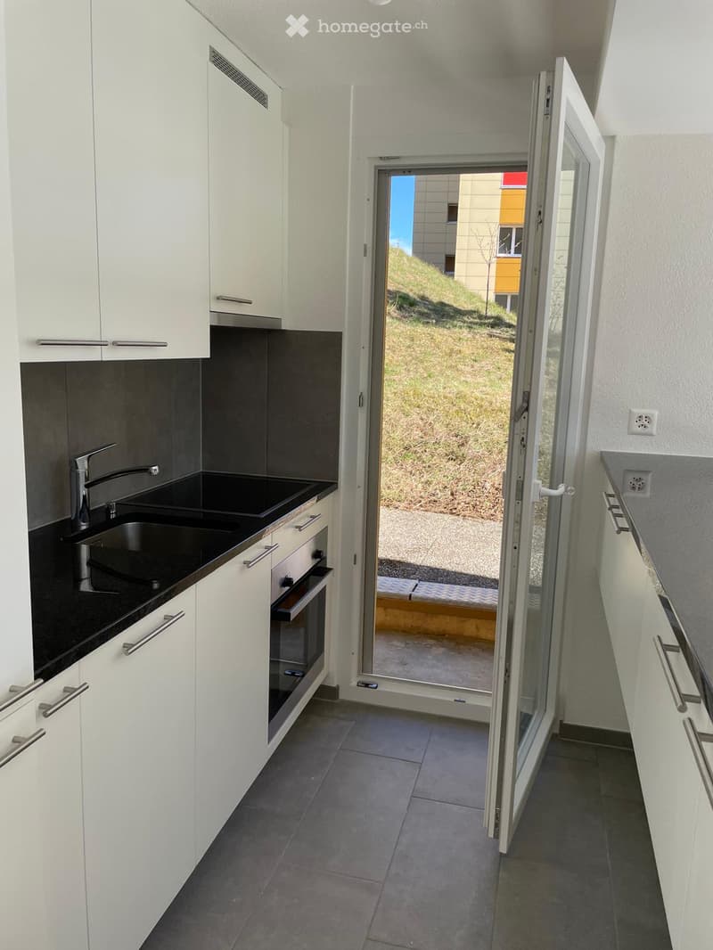 modern kitchen with white cabinets, black countertops, stainless steel sink, oven, and faucet, open door to outdoor view