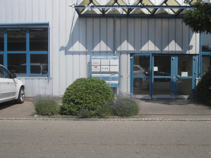 Metal exterior, white and blue windows, double doors, bushes, a car parked in front