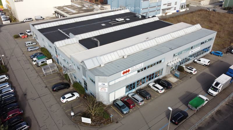 Warehouse building with ample parking space, multiple garages visible, rooftop solar panels, entrance with signage