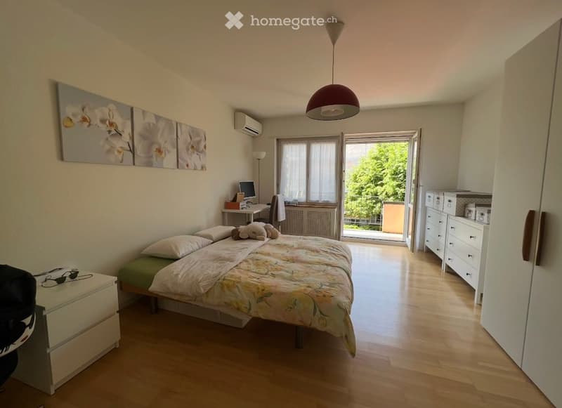 Bedroom with bed, desk, chair, monitor, lamp, air conditioner, paintings, wardrobe, drawers, balcony