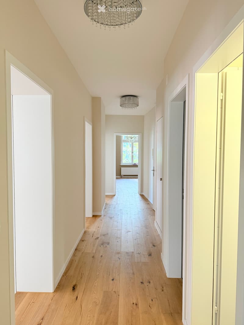 Corridor / Hallway. Empty hallway with wooden floors and white walls, two chandeliers, and doors on both sides.