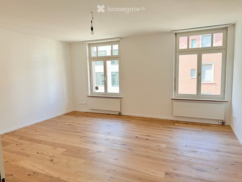 Unfurnished Room. Empty room with white walls, wooden floor, and two large windows. There are white radiators below the windows.