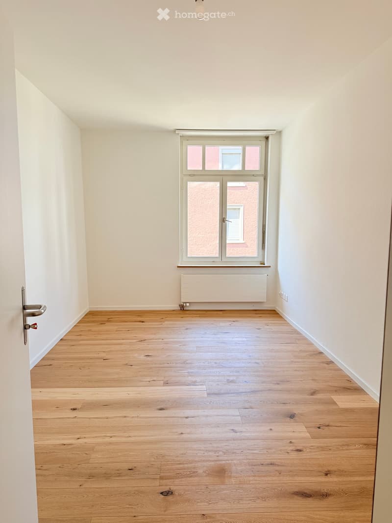 Unfurnished Room. An empty room with white walls, wooden floor, and a window with a view of a building.
