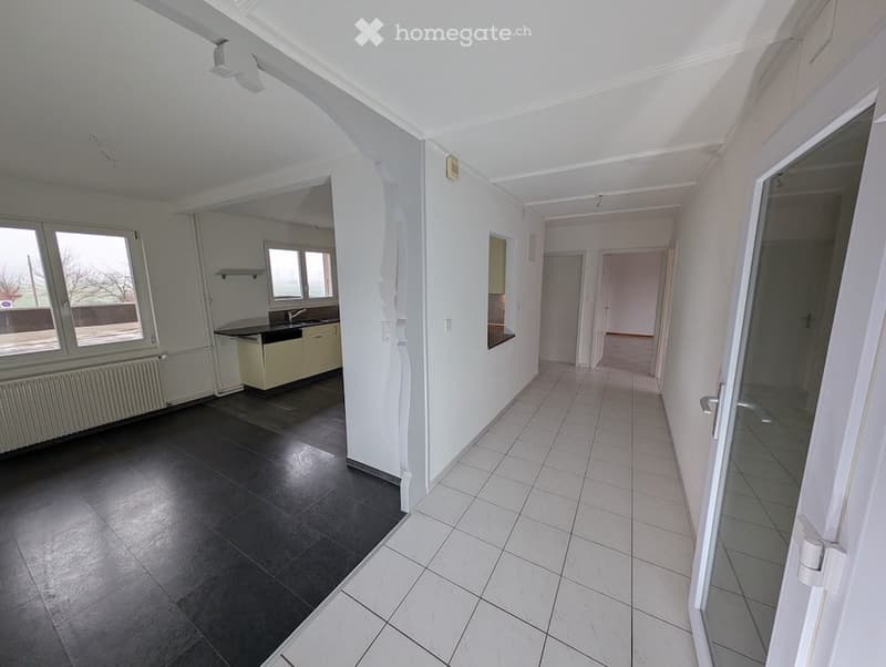 tiled floor, white walls, kitchen area with sink and cabinets, two large windows, door leading to another room