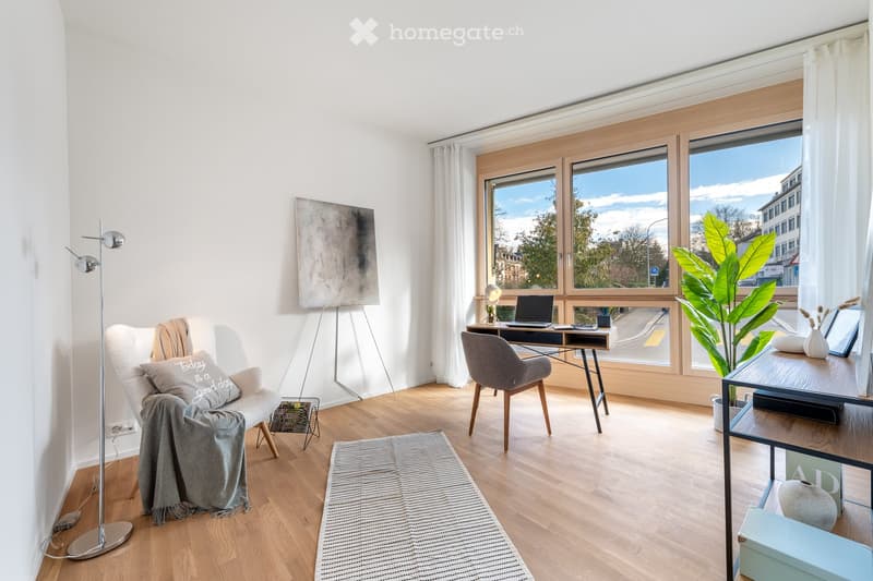 modern room with wooden floor, white walls, desk, chair, floor lamp, rug, chair with blanket, painting, plant, large windows