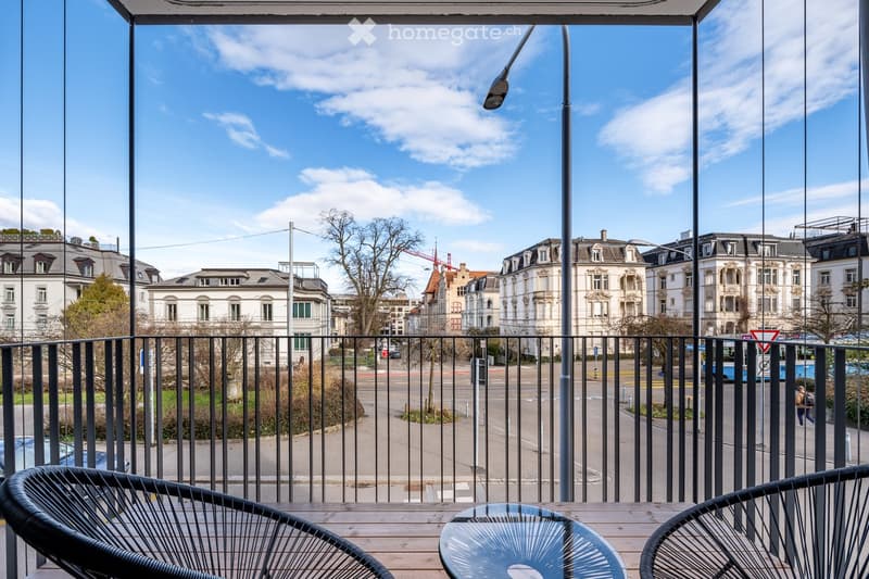 Balcony with a view of the city, two chairs, a table, and a black railing
