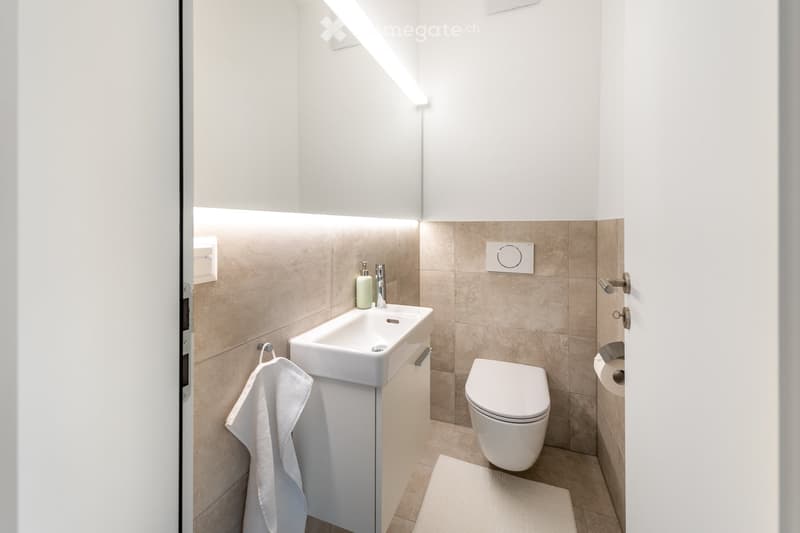 modern bathroom with white sink, white toilet, beige tiles, white towel, white rug