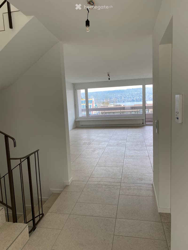 Empty room with white walls, tiled floor, large window with view, metal railing on stairs