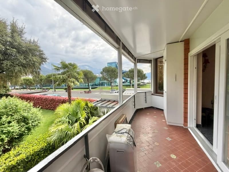 Balcony with tiled floor, large windows, view of the city, plants, and trees