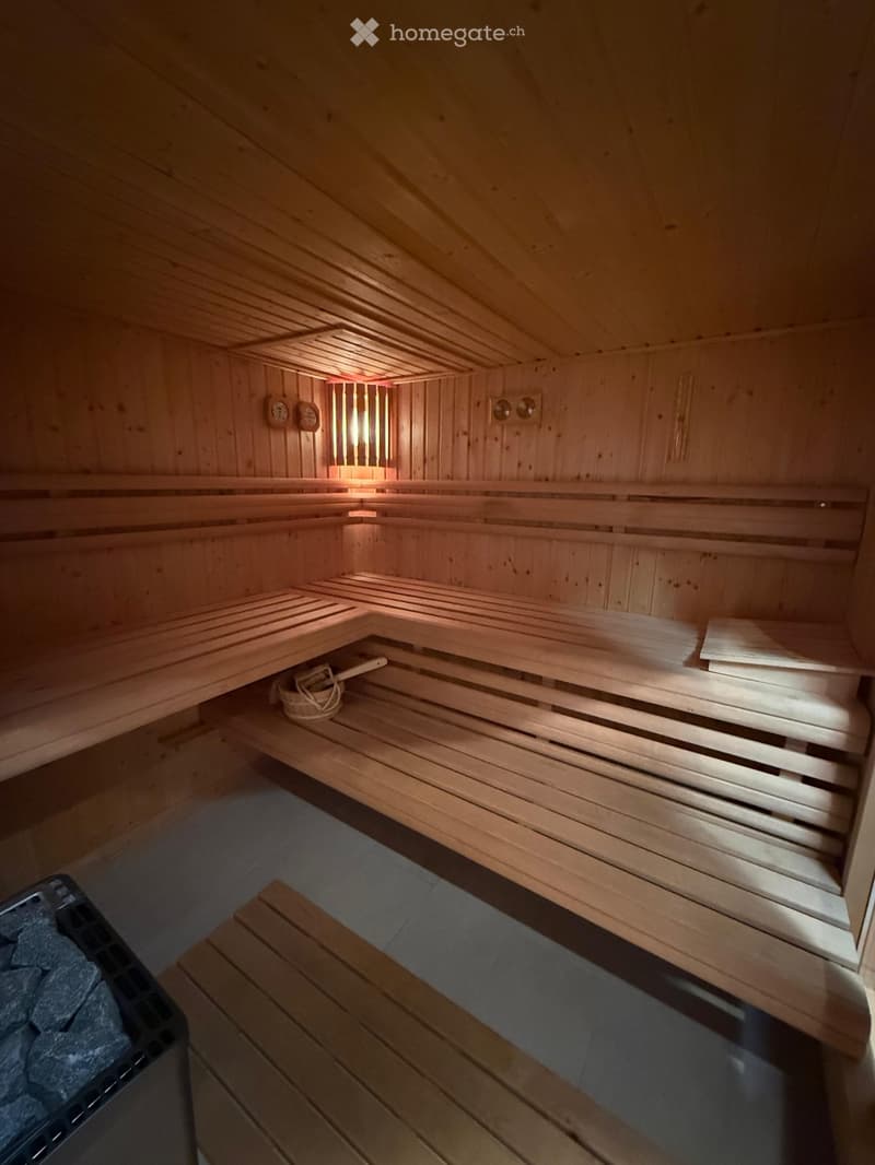 A wooden sauna with multiple wooden benches, a stone stove, and a small wooden basket on the floor.