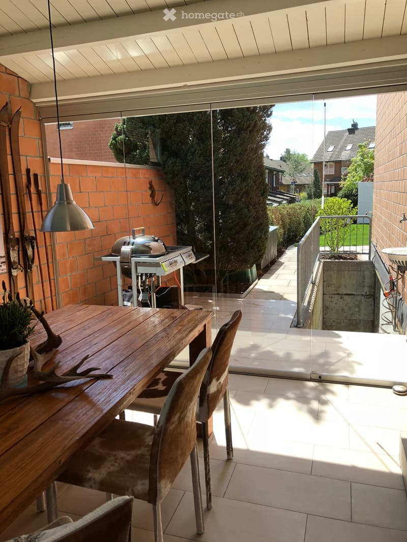 dining area with wooden table, chairs, brick wall, glass door, outdoor grill, potted plant, lamp
