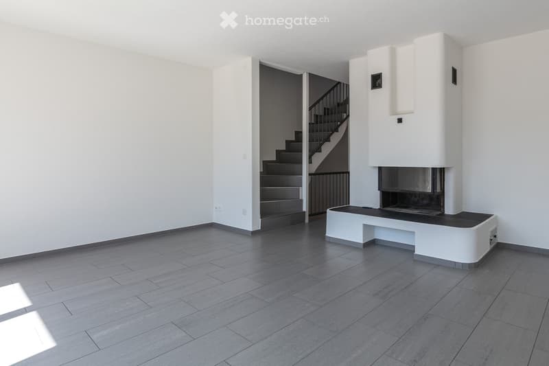Empty room with white walls, gray floor, fireplace, staircase