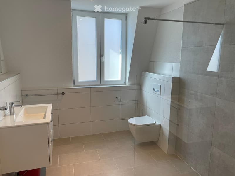 Modern bathroom with white tiles, white sink, glass shower enclosure, toilet, large window.