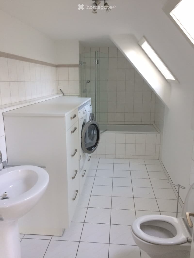 Bathroom with white tiles, white sink, white toilet, white washing machine, glass shower enclosure, bathtub, white cabinets