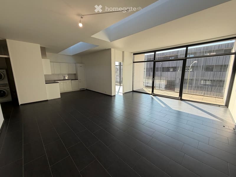 Open floor plan, modern kitchen, large windows, black tiled floor, white walls, ceiling lights, washing machine