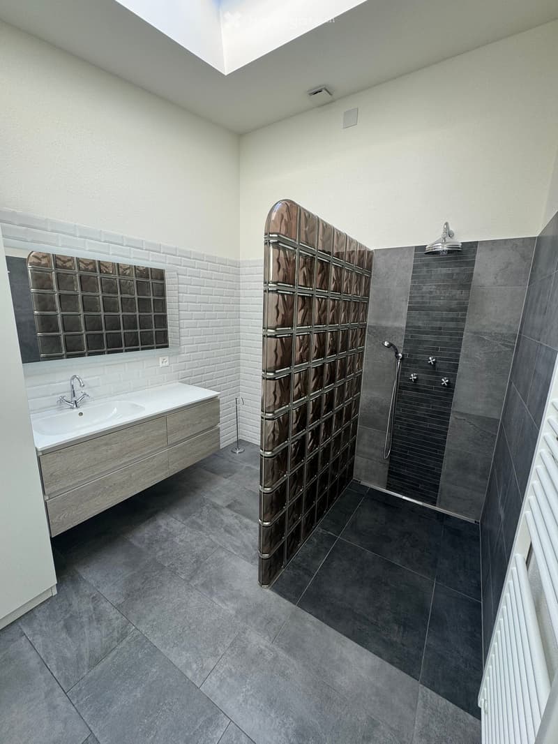 modern bathroom with white and gray tiles, a sink with a faucet, a shower with a glass partition, and a mirror