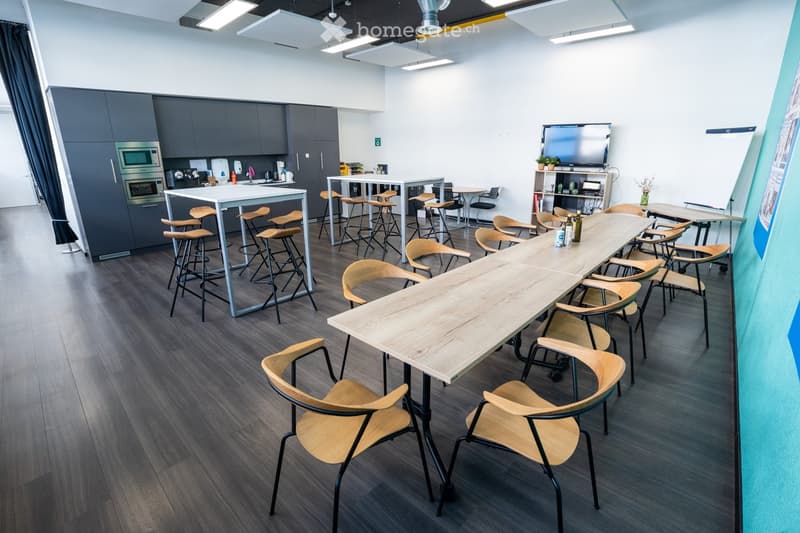 modern kitchen area with appliances, long tables, chairs, tv, whiteboard