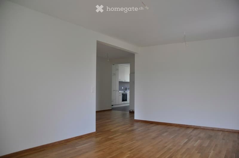 Empty room, hardwood floors, white walls, open archway leading to kitchen