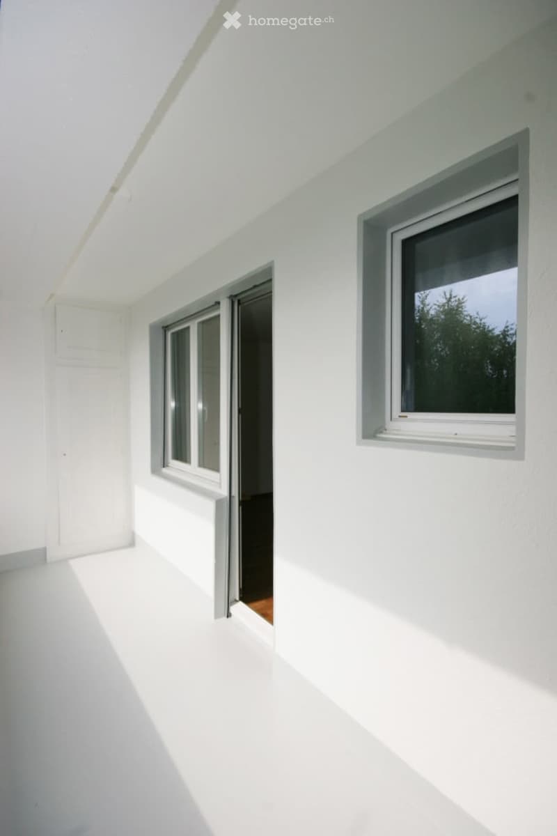 Empty room, white walls, white floor, open door to balcony, two windows