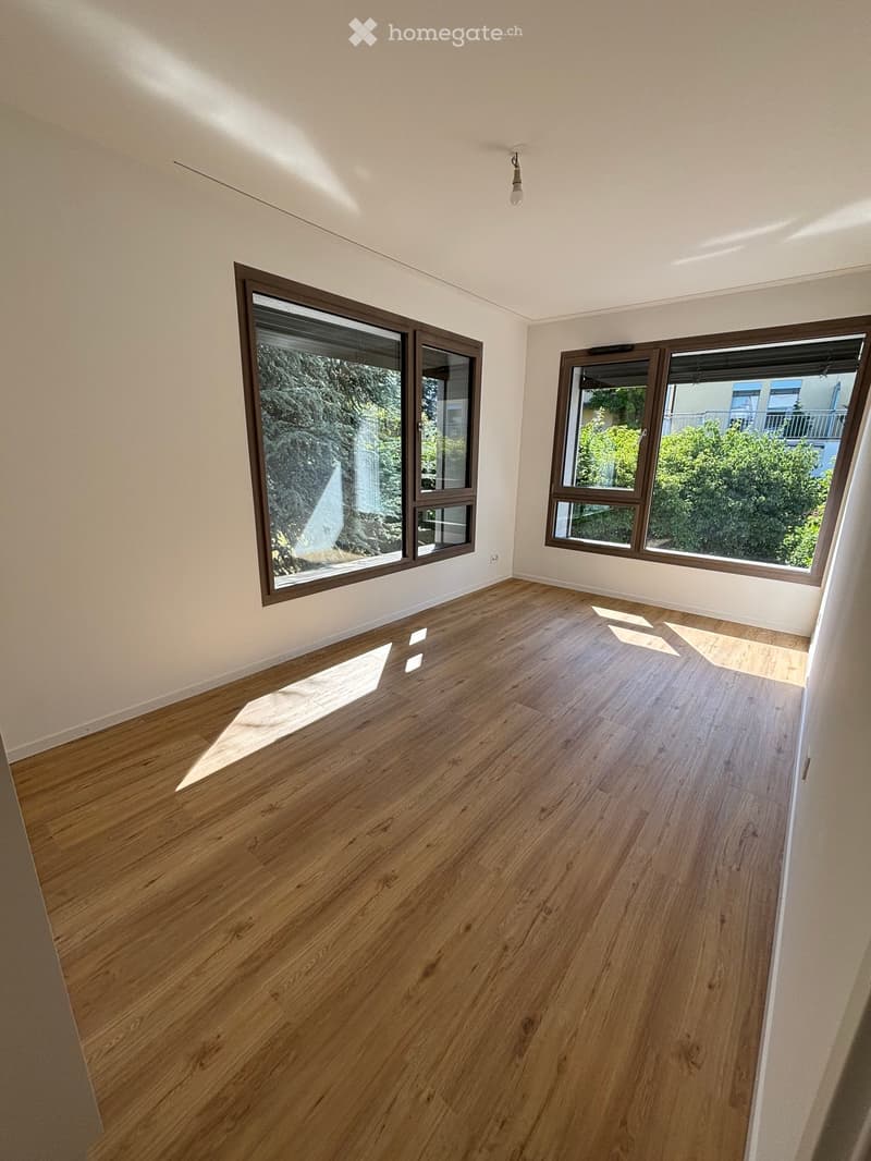 Empty room with wooden flooring and large windows, allowing natural light to fill the space.