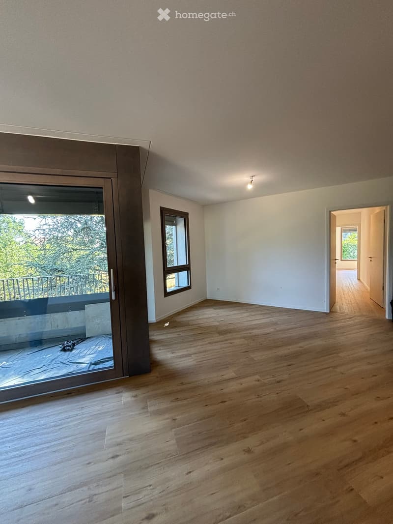 Empty room with wooden flooring, large sliding glass door leading to a balcony, and a small window on the adjacent wall.