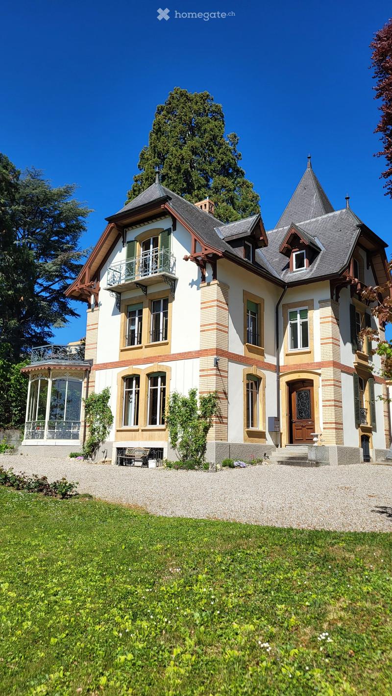 3 story house, white and brown exterior, large windows, balcony, gravel driveway, garden
