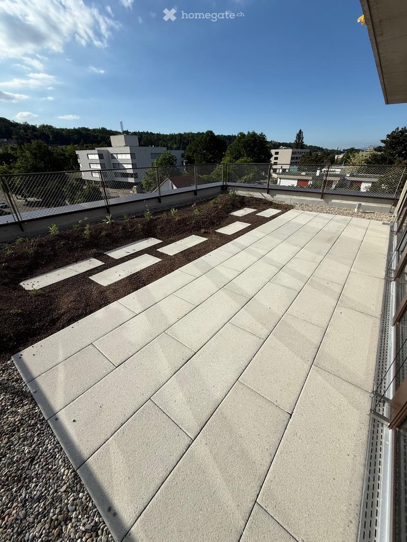 Rooftop garden with paved tiles, gravel, plants, and a fence