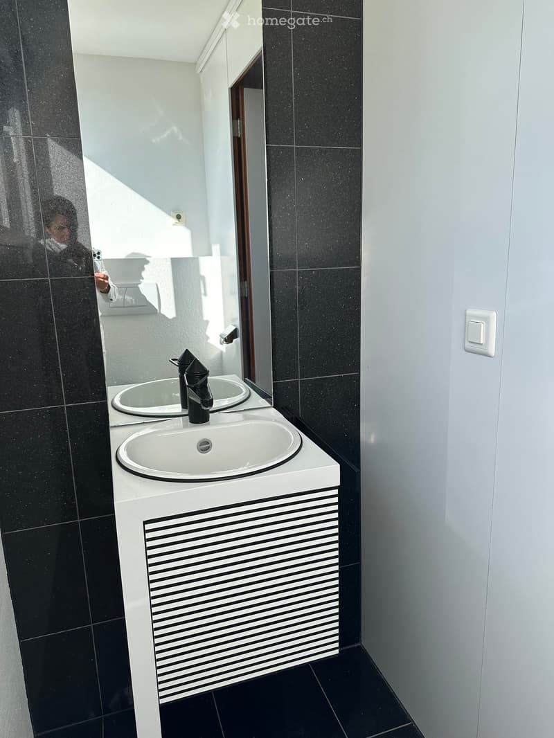 Bathroom with a double sink, mirror, and black tiles