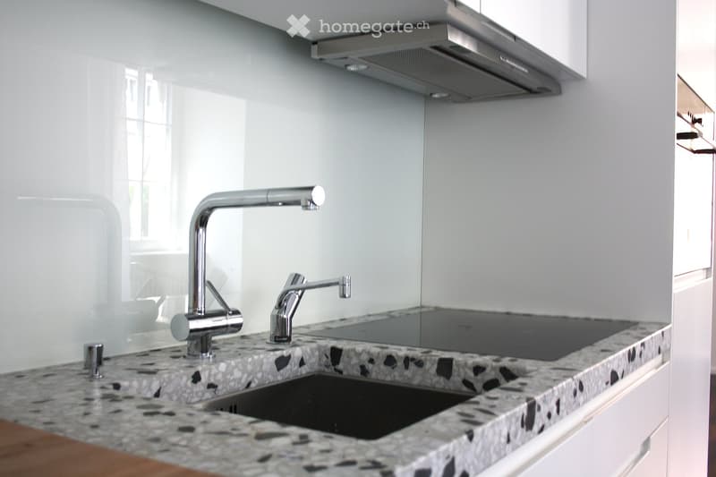 Modern kitchen with a granite countertop, stainless steel faucet, and a sleek exhaust hood.