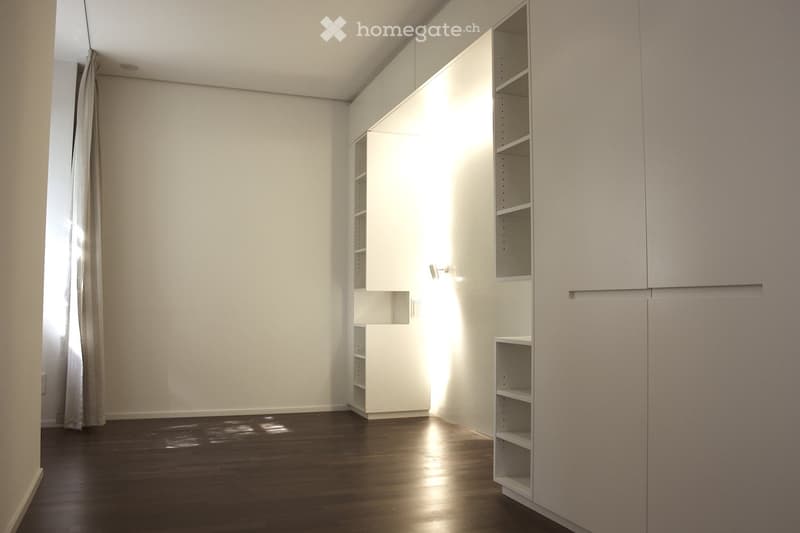 An empty room with white walls, wooden floor, and built-in white cabinets.
